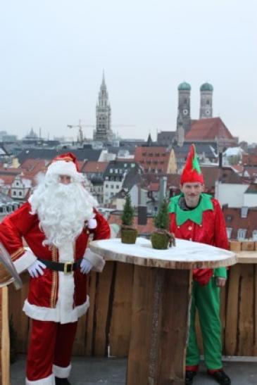 Weihnachtsmann und Elf hoch über den Dächern von München